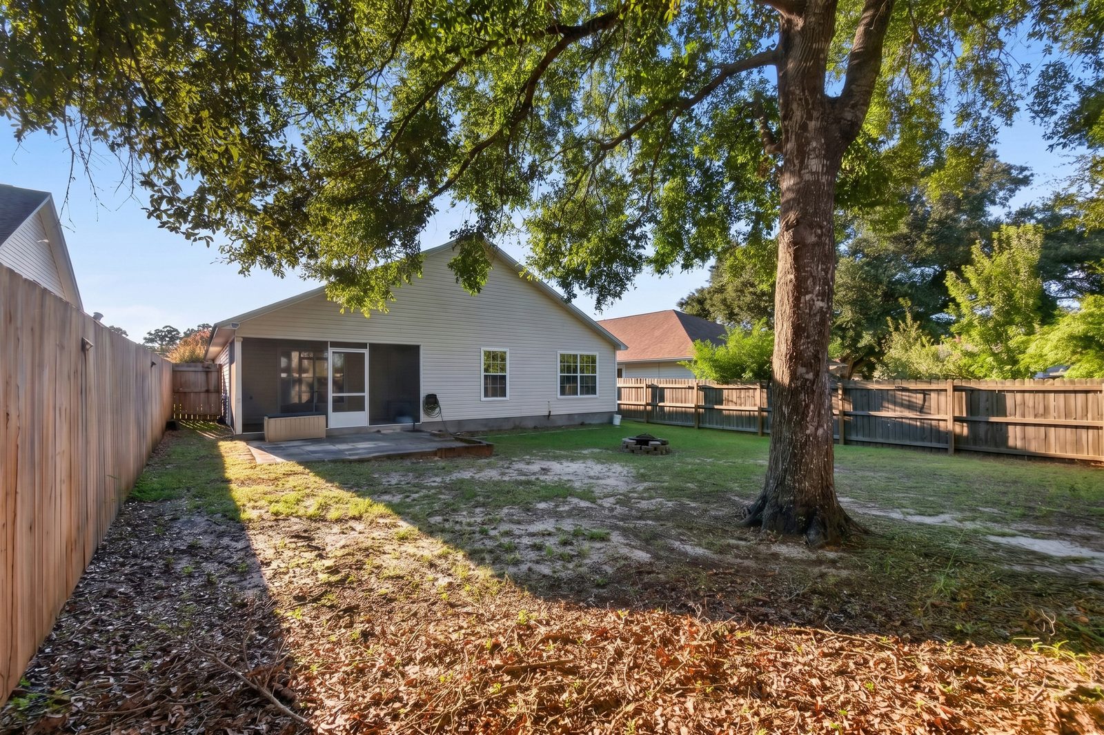 Backyard from the far fence: the back of the house with its screened porch and paver patio, a fire pit, and a large shade tree